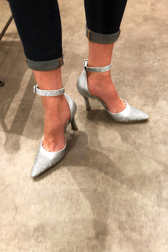 Light silver women's open side shoes, with a strap around the ankle. Tapered toe. Very high spool heels. Worn view - Florence KOOIJMAN